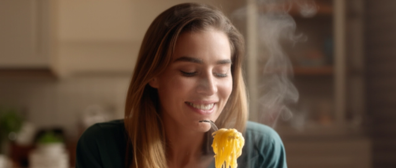 Una donna caucasica sorride mentre gusta un piatto di pasta ai quattro formaggi in un ambiente caldo e accogliente.